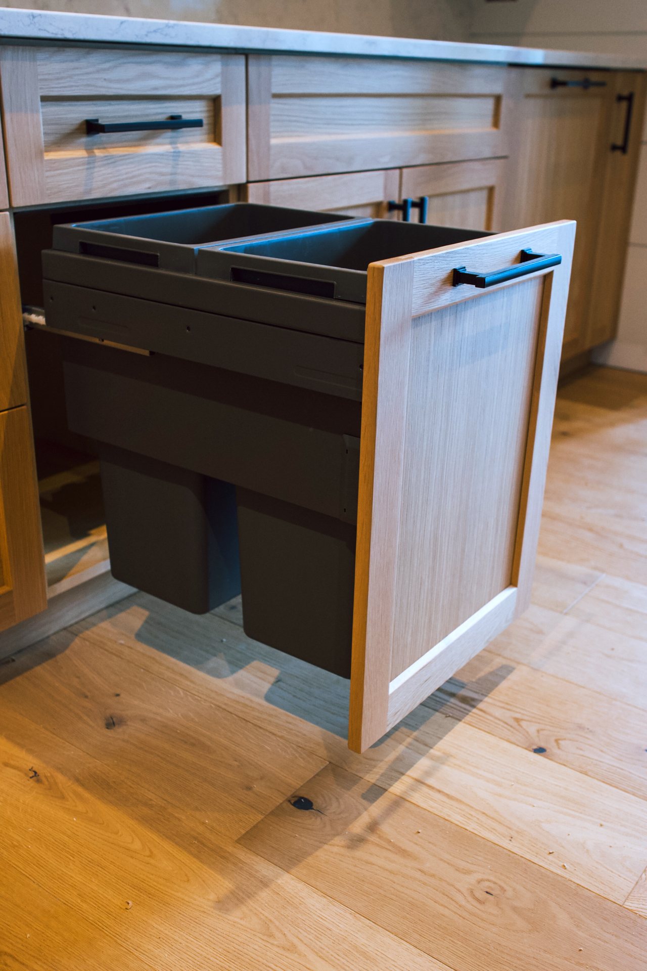 Integrated waste and recycling pull-out behind a white oak door