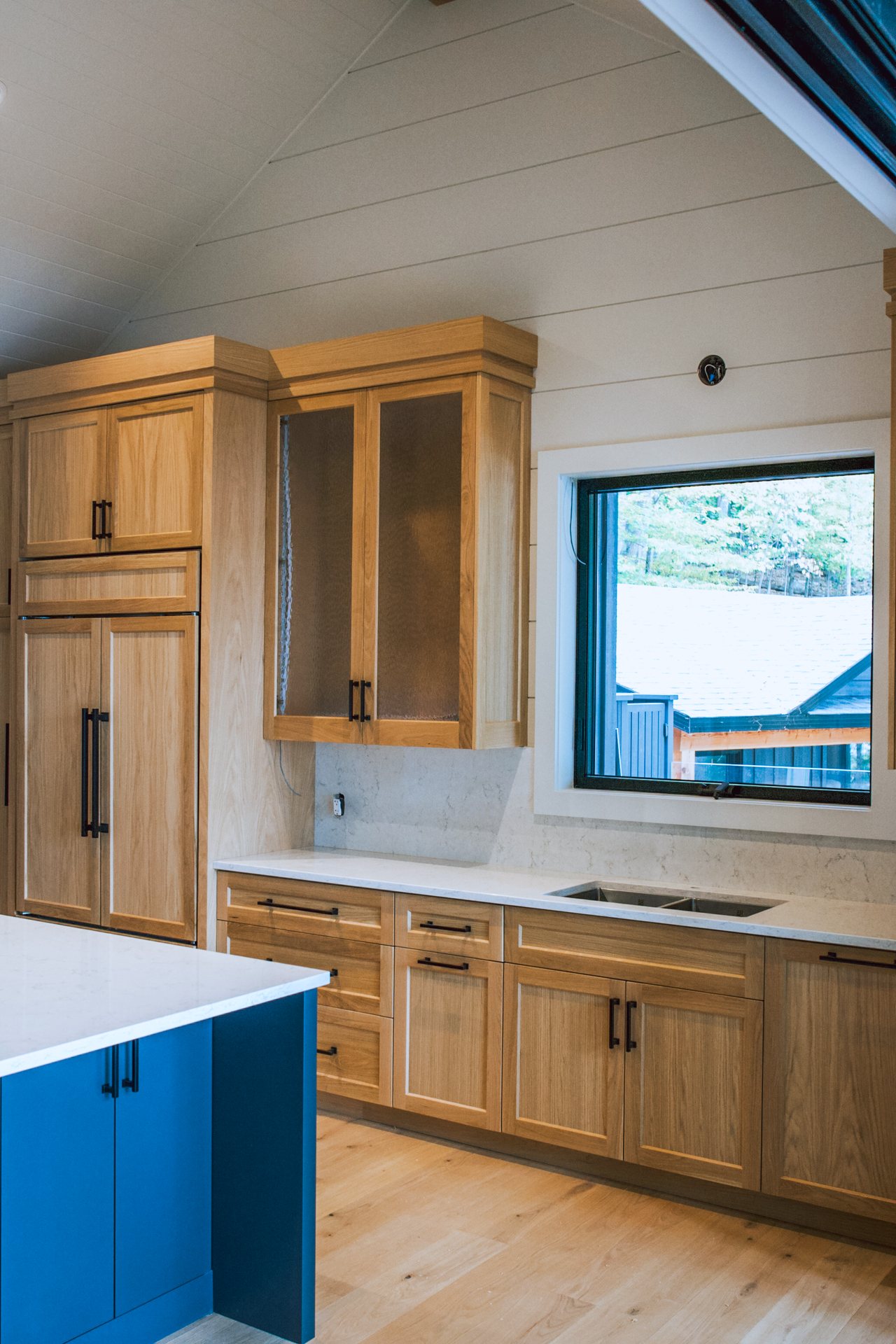 White oak sink wall with textured glass uppers, white marble counters and painted island