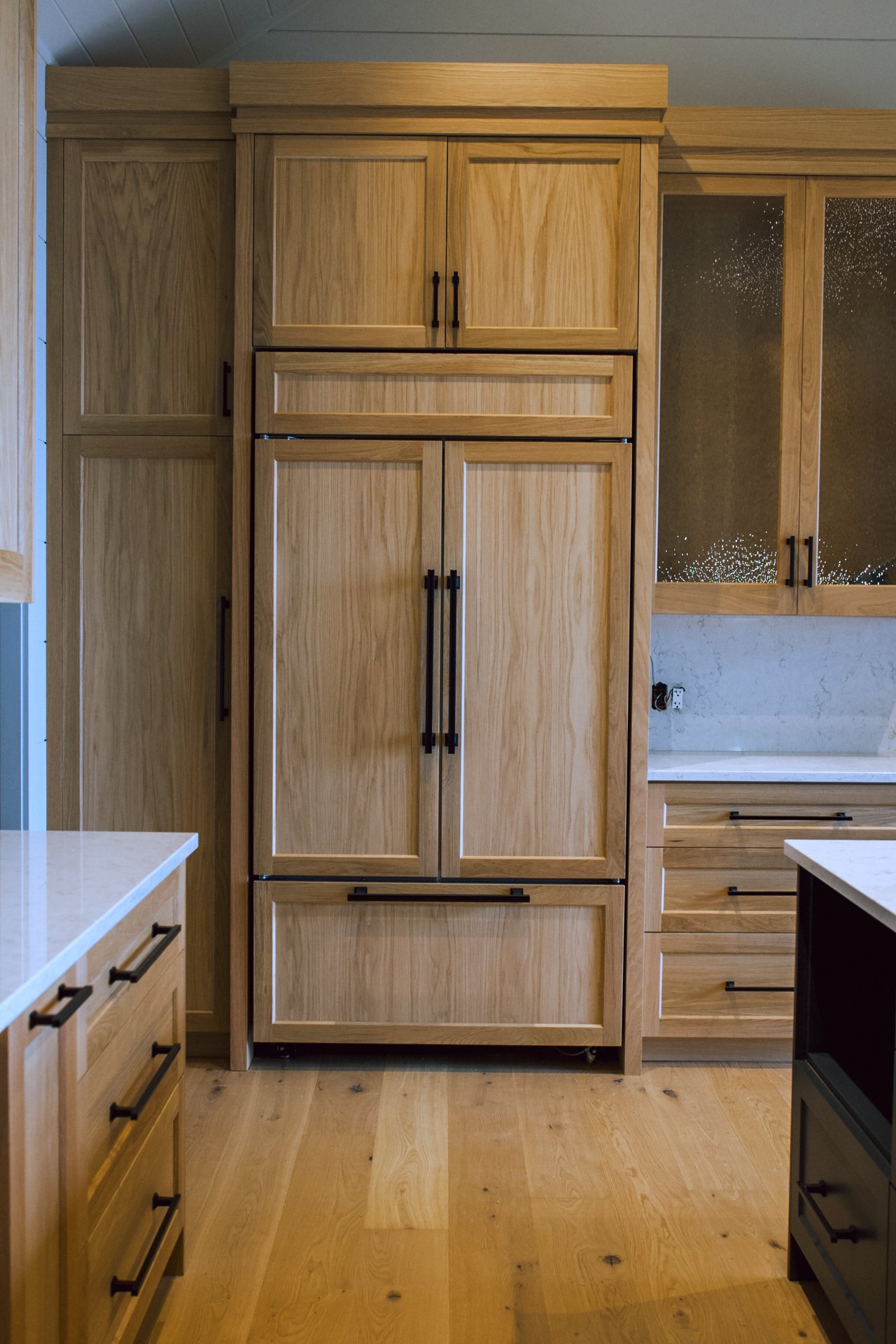 Oak panelled refrigerator set into a white oak pantry wall with textured glass uppers