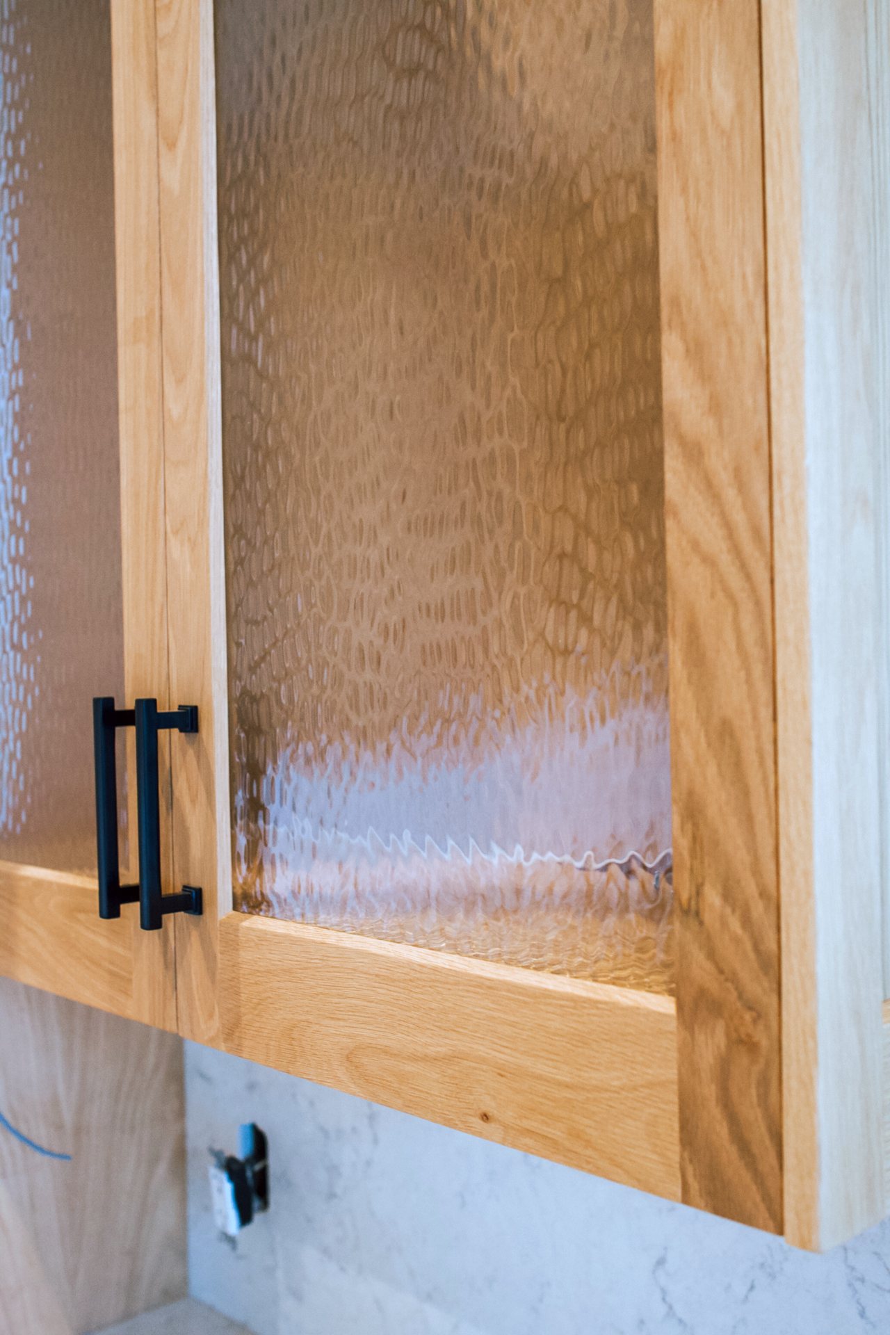 Textured glass door in a white oak upper cabinet with black pull