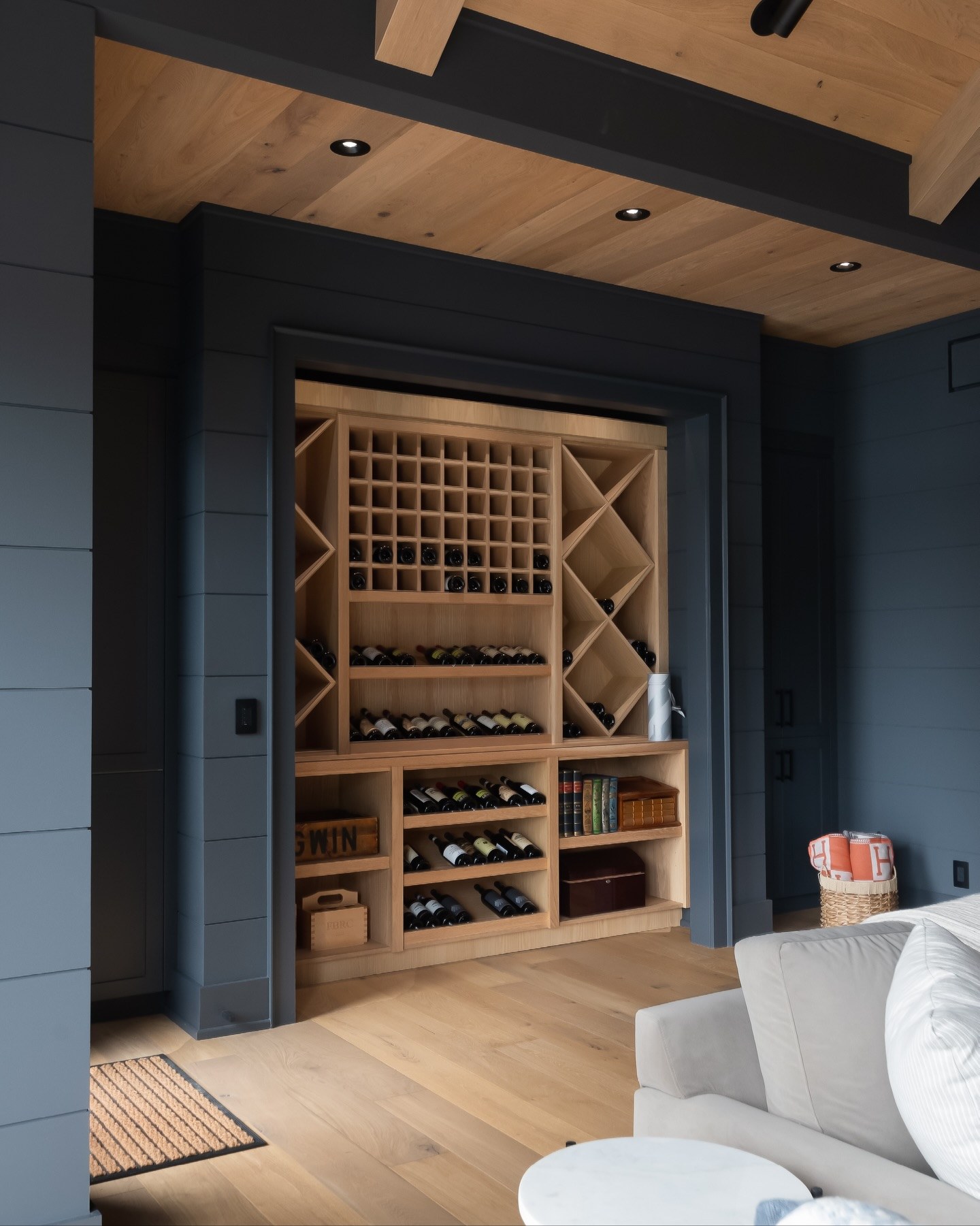 Built-in white oak wine wall with diamond bins and display shelving, recessed into charcoal panelling, Bigwin Island cottage